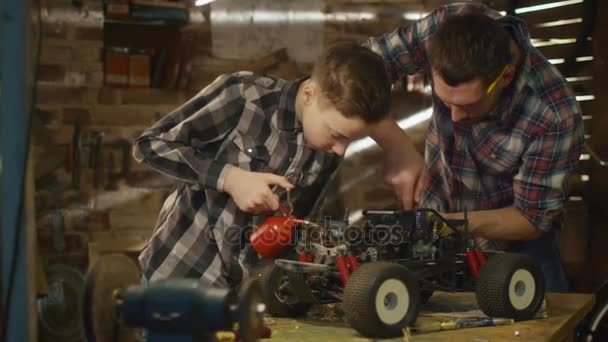Far och son arbetar på en radio kontroll leksaksbil i ett garage hemma. — Stockvideo