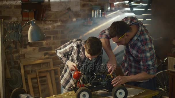 Отец и сын работают над радиоуправляемой игрушечной машиной в гараже дома. . — стоковое видео