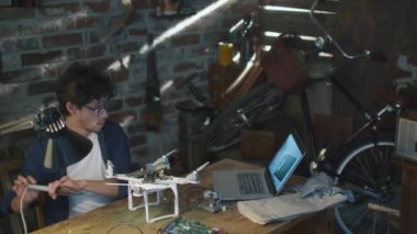 Öğrenci dizüstü bilgisayar denetlenirken bir garaj bir dron olarak elektrik bileşenleri lehimleme.
