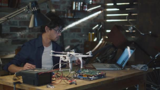 El hombre está soldando componentes eléctricos en un dron en un garaje mientras revisa una computadora portátil . — Vídeos de Stock