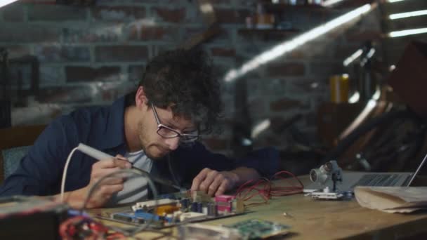 Студент вивчає електроніку і паяє друковану плату в гаражі . — стокове відео