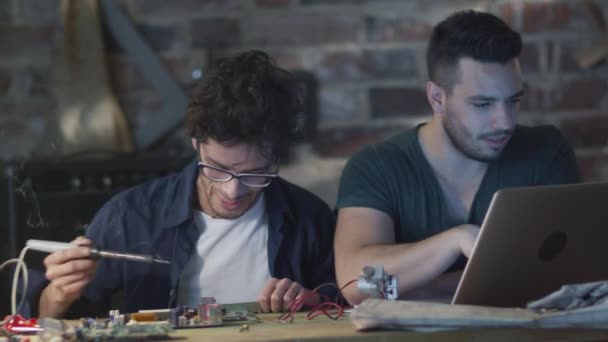 Twee studenten studeren elektronica en solderen in een garage. — Stockvideo