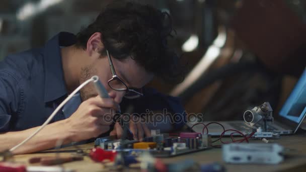 Estudante está estudando eletrônica e soldando uma placa de circuito em uma garagem . — Vídeo de Stock