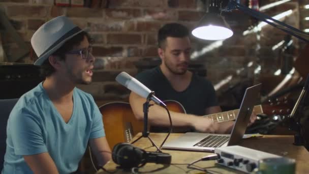 Deux jeunes hommes chantent et jouent de la guitare tout en enregistrant une chanson dans un home studio dans un garage . — Video