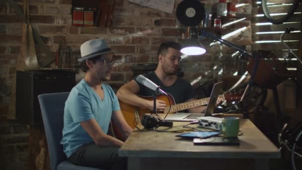 Dos jóvenes cantan y tocan la guitarra mientras graban una canción en un estudio en un garaje . — Vídeos de Stock