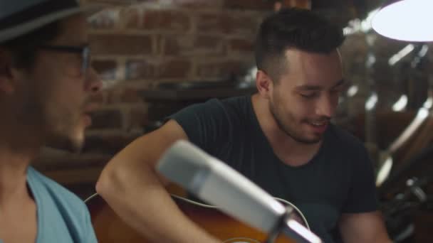 Двоє молодих людей співають і грають на гітарі під час запису пісні в домашній студії в гаражі . — стокове відео