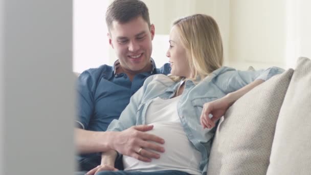 Gravid blond kvinna och en man koppla av på en soffa hemma. — Stockvideo