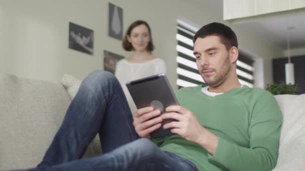 对幸福的夫妇是坐在家里的沙发上，使用一台平板电脑. — 图库视频影像