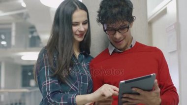 Beyaz kız ve Hispanik erkek öğrencilerin bir üniversite koridorda bir tablet bilgisayar kullanın.