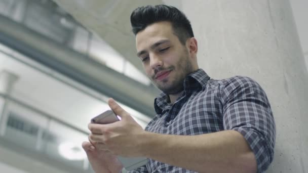 Portrét mladé hispánský mužské studenta pomocí smartphone na univerzitní chodbě. — Stock video