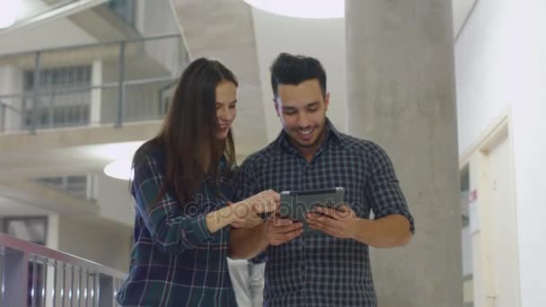 白种人的女孩和一个西班牙裔的男同学在大学的走廊里使用一台平板电脑. — 图库视频影像