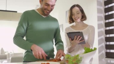 Mutlu çift evde mutfakta sağlıklı yiyecek bir tablet bilgisayar denetlenirken hazırlanıyor.