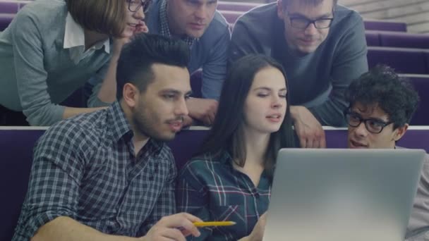 Grupo de estudantes do sexo feminino e masculino estão sentados em uma sala de aula da faculdade e olhando para um computador portátil . — Vídeo de Stock