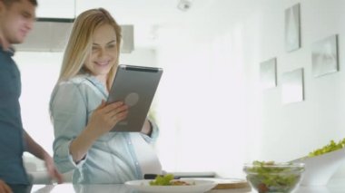 Hamile kadın evde mutfakta sağlıklı yemek hazırlarken bir tablet bilgisayar kullanıyor.