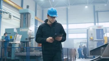 Fabrika işçisi kask içinde yürüyüş ve bir tablet bilgisayar kullanarak.