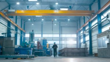 Fabrika işçisi kask içinde endüstriyel tesisler yürüyor.