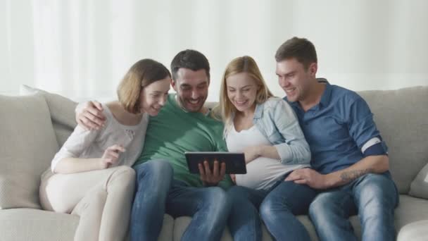 Des amis sont assis sur le canapé à la maison et utilisent la tablette pour se divertir . — Video