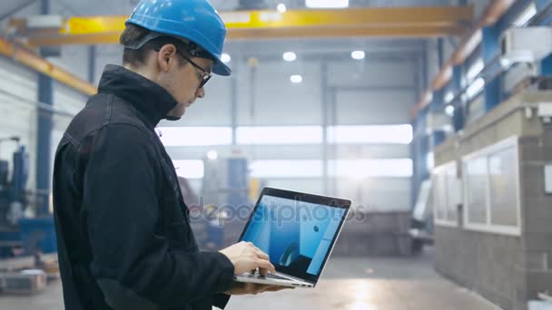 Trabalhador da fábrica em um chapéu duro está usando um computador portátil com um software de engenharia . — Vídeo de Stock