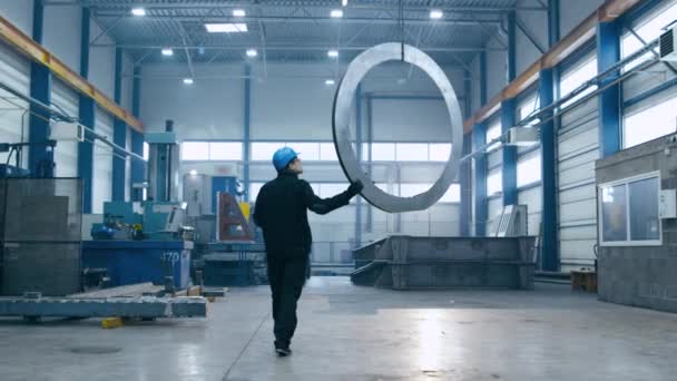 Trabajador de fábrica en un sombrero duro está moviendo un detalle de metal con una grúa remota . — Vídeo de stock