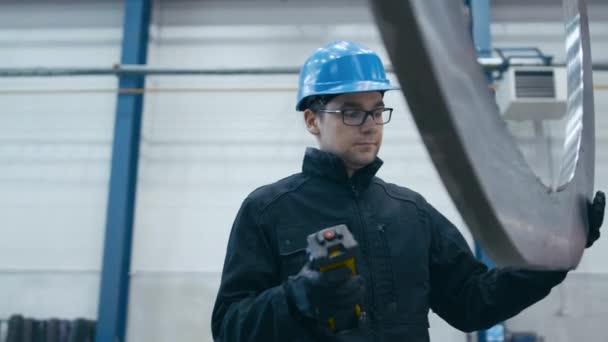 Fabriksarbetare i en hård hatt går en metall detalj med en remote kran. — Stockvideo