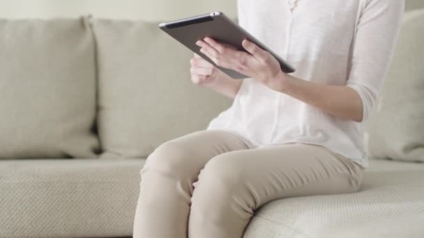 Mooie jonge vrouw is met behulp van een tablet-pc zittend op een bank thuis. — Stockvideo