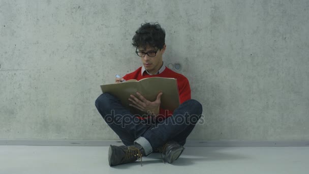 Латиноамериканец сидит в коридоре колледжа и читает учебник . — стоковое видео