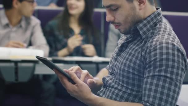 İspanyol erkek öğrenci üniversite sınıfta bir tablet bilgisayar kullanıyor. — Stok video