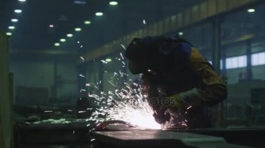 Sıcak sparks bir sonucunda üretilen ağır sanayi işçisi bir fabrikada metal ile açı değirmeni üzerinde çalışıyor.