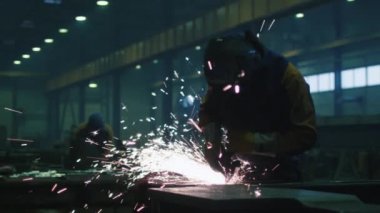 Sıcak sparks bir sonucunda üretilen ağır sanayi işçisi bir fabrikada metal ile açı değirmeni üzerinde çalışıyor.