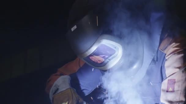 Heavy industry worker at a factory is welding metal in dark interior. — Stock Video