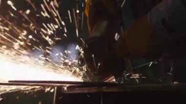 Sıcak sparks bir sonucunda üretilen ağır sanayi işçisi bir fabrikada metal ile açı değirmeni üzerinde çalışıyor.