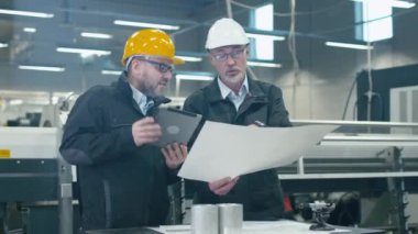 Bir fabrikada bir tablet bilgisayardaki bilgileri denetlenirken bir plan iki mühendis tartışmak.