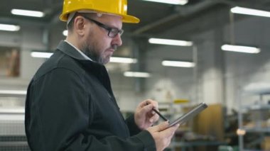 Kask içinde kıdemli mühendis bir fabrikada bir ekran kalemi ile bir tablet bilgisayar kullanıyor.