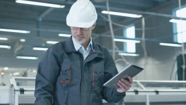 Ingeniero senior en hardhat está utilizando una tableta en una fábrica . — Vídeos de Stock