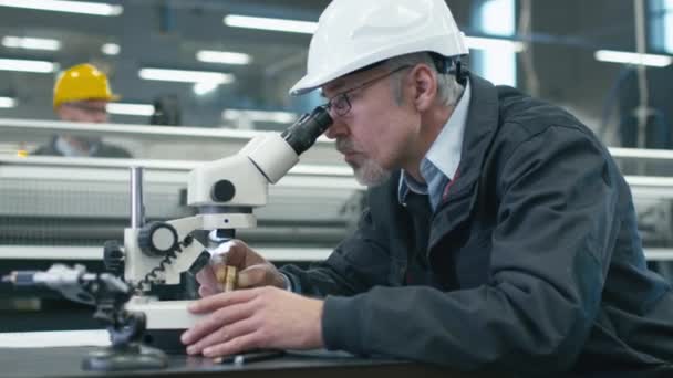 Senior engineer is inspectie van een detail onder Microscoop in een fabriek. — Stockvideo