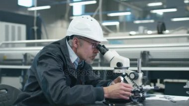 Kıdemli mühendis bir detay bir fabrikada mikroskop altında incelemek.