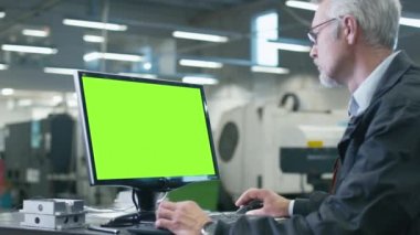 Bardaklarda kıdemli mühendis bir masaüstü bilgisayara bir monitörde yeşil bir ekran ile çalışma.