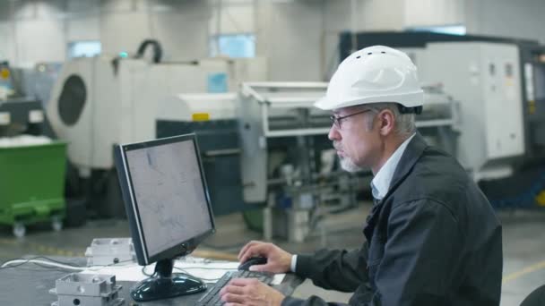 Senior engineer in glasses is working on a desktop computer with a green screen on monitor in a factory. — Stock Video