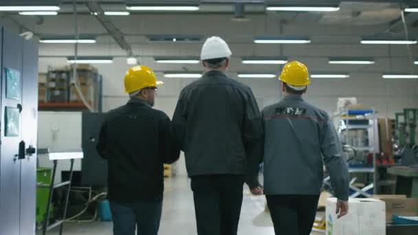 Achteraanzicht van senior ingenieur en twee werknemers lopen met papieren door de fabriek-ruimte. — Stockvideo