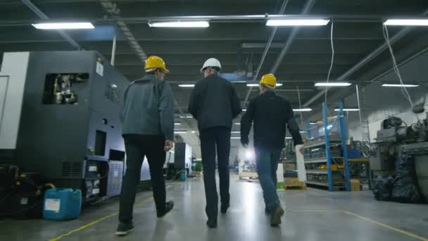 Back view of senior engineer and two workers are walking with papers through the factory space. — Stock Video