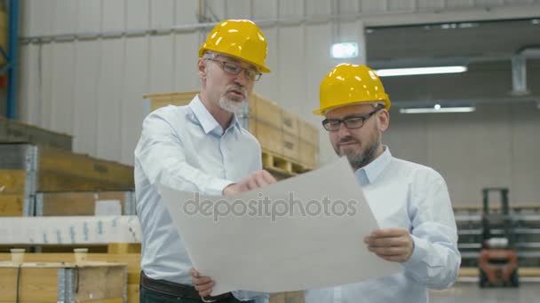 Dos empleados en el almacén del centro logístico hablan sobre el plan en el libro blanco . — Vídeos de Stock