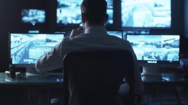 Karanlık bir izleme odada bir bilgisayarda çalışma göstermek perde ile dolu iken güvenlik görevlisi kahve içiyor.