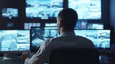 Karanlık bir izleme odada bir bilgisayarda çalışma göstermek perde ile dolu iken güvenlik görevlisi kahve içiyor.