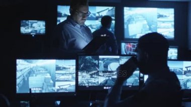 Güvenlik görevlisi karanlık bir izleme odada göstermek perde ile dolu bir tablet bilgisayar kullanıyor.