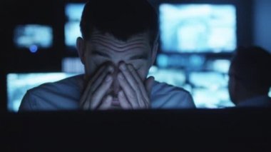 Yorgun ve stresli güvenlik görevlisi karanlık bir izleme odada göstermek perde ile dolu bir bilgisayarda çalışıyor.