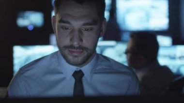 Odaklı güvenlik görevlisi karanlık bir izleme odada göstermek perde ile dolu bir bilgisayarda çalışıyor.