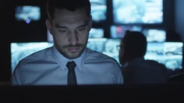 Odaklı güvenlik görevlisi karanlık bir izleme odada göstermek perde ile dolu bir bilgisayarda çalışıyor.