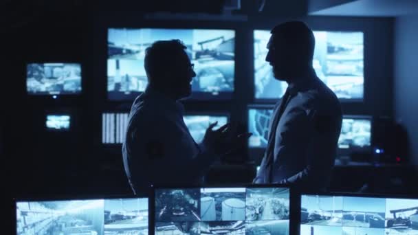 Zwei Sicherheitsbeamte unterhalten sich in einem dunklen Überwachungsraum mit Bildschirmen. — Stockvideo