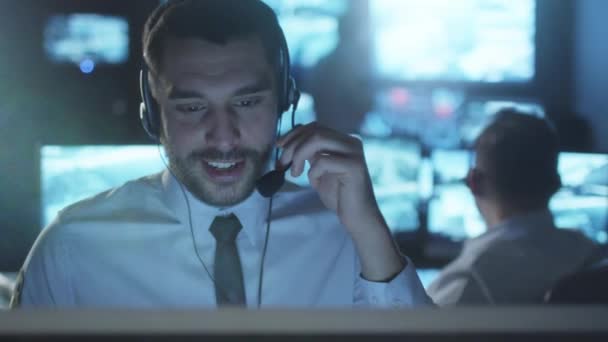 Spécialiste du support technique parle sur un casque tout en travaillant sur un ordinateur dans une salle de surveillance sombre remplie d'écrans d'affichage .