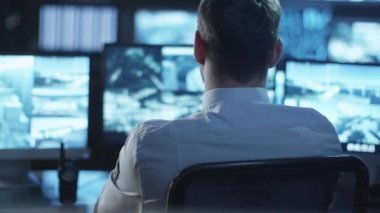 Mutlu ofis çalışanı Beyaz gömlekli dönüyor uzak bir bilgisayar, kamera ve karanlık bir izleme odada dolu gülümsüyor bakar ekranları görüntülemek.